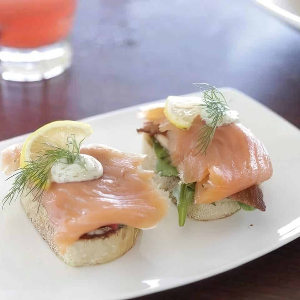 Two smoked salmon crostini with dill, cream cheese, and lemon on a white plate.
