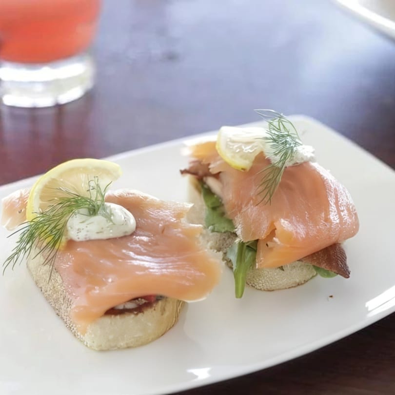 Two smoked salmon crostini with dill, cream cheese, and lemon on a white plate.