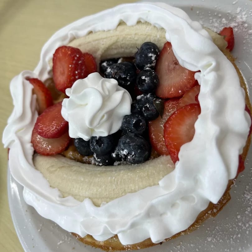 A waffle topped with sliced bananas, blueberries, strawberries, and whipped cream from Lighthouse Cafe.