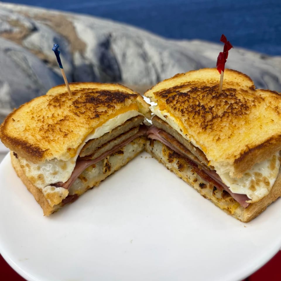 Grilled breakfast sandwich with ham, egg, and cheese, cut in half, on a white plate.