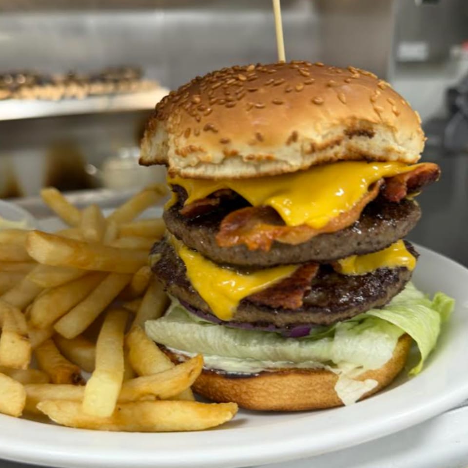 Double cheeseburger with bacon, lettuce, and fries on a white plate.