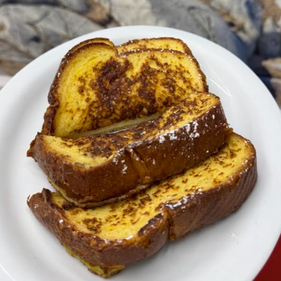 Three slices of golden-brown French toast, dusted with powdered sugar, on a white plate.